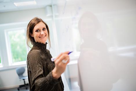 Kvinne som smilar i kamera, står ved whiteboard